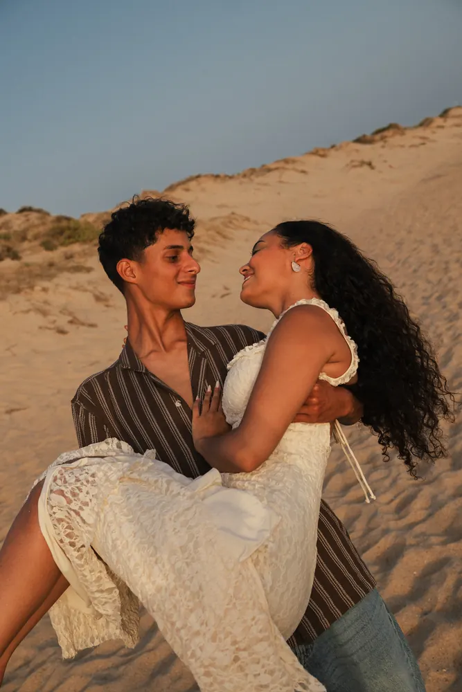 Noivo a pegar a noiva ao colo numa duna dourada ao pôr do sol, elopement no Algarve