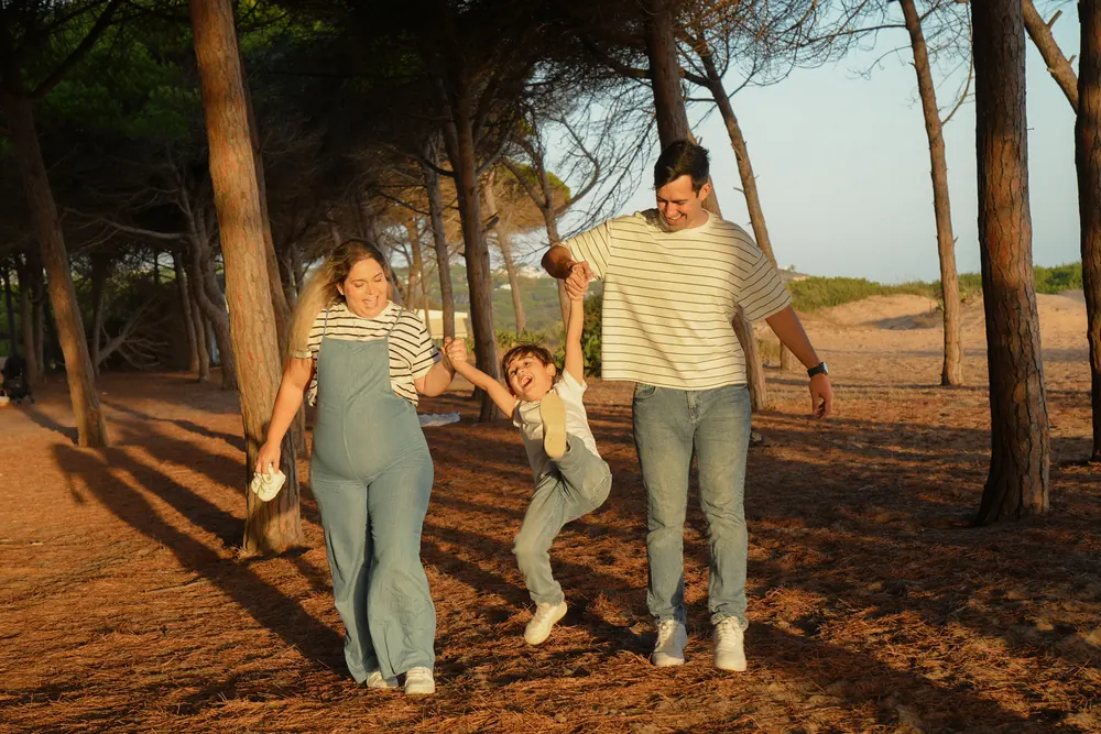 Pais a baloiçar o filho pelos braços num pinhal junto à praia, ao fim do dia no Algarve