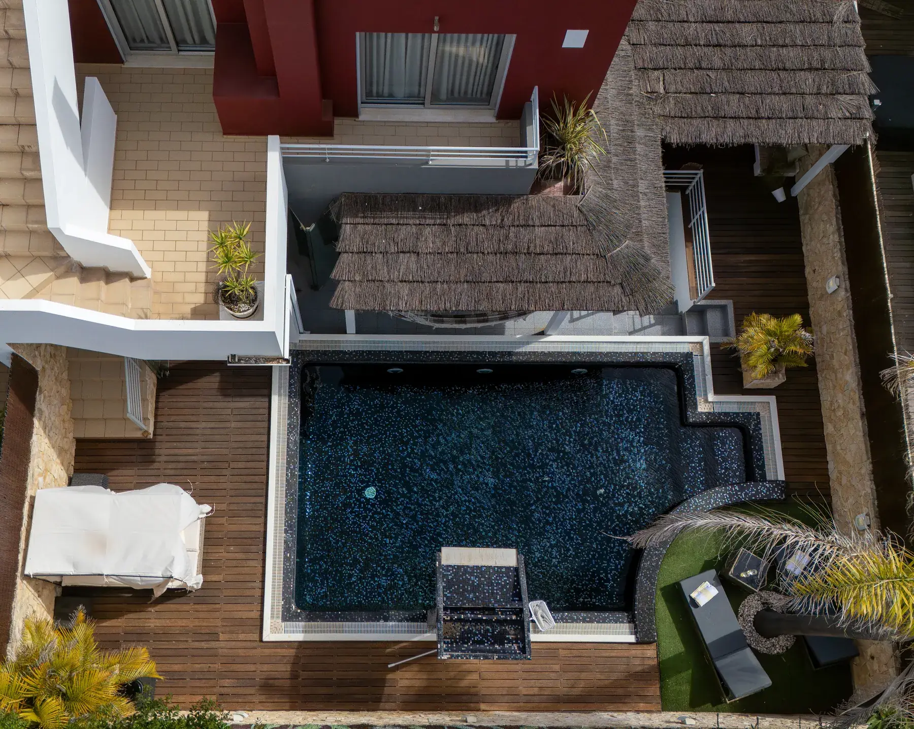 Vista aérea de uma villa no Algarve com piscina de mosaico escuro, deck de madeira e palhota